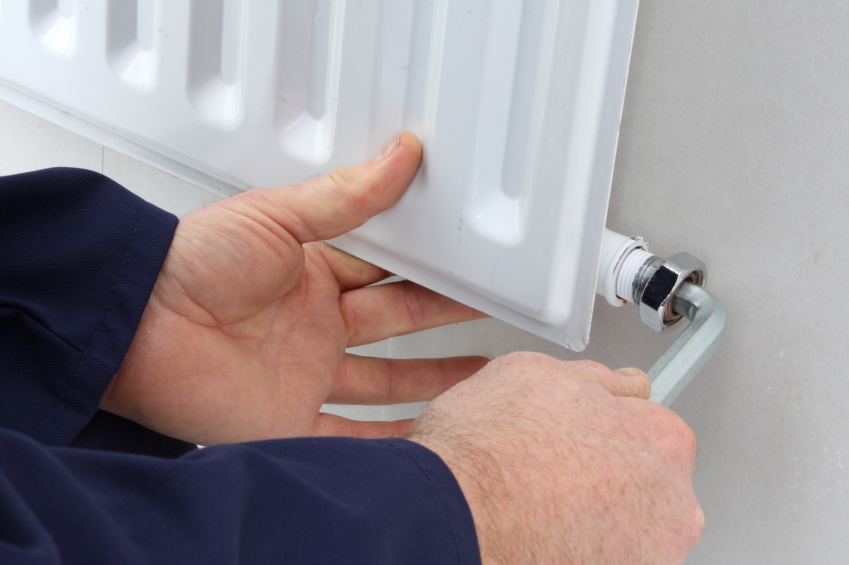 Man readjusting the valve on a radiator to make it bleed